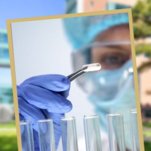 A researcher wearing full protective gear holds a pill using tweezers above a row of test tubes.